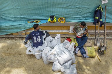 Cartagena, Colombia - July 25, 2023: 2 Workers take lunch break while repairing border wall of Parque del Centenario.  clipart