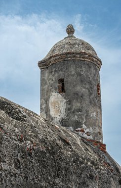 Cartagena, Kolombiya - 25 Temmuz 2023: Surların üzerine inşa edilmiş eski gri taş gözcü kulesi, mavi bulutların altında saat kulesiyle eski kasaba girişinin batısına doğru adım atıyor.