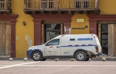 Cartagena, Colombia - July 25, 2023: White Brinks security van in front of Bancolombia office on Plaza de la Aduana. Brown-ochre facade with brown trim around doors and windows clipart