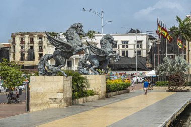 Cartagena, Kolombiya - 25 Temmuz 2023: Çifte Pegasus heykelleri eski kasaba rıhtımının sonunda ve arkasında mimari binalar var. Ulusal bayraklar arkasında