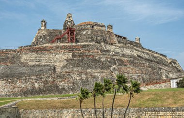 Cartagena, Kolombiya - 25 Temmuz 2023 San Felipe de Barajas Kalesi tepeden tırnağa duvar örer. Mavi bulutlara karşı. Çimenler ve yeşil yapraklar önde.