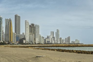 Cartagena, Kolombiya - 25 Temmuz 2023 Bocagrande yarımadasının batı kıyısında, mavi bulutların altında uzun ve modern binaları var. Kumsal Karayip denizinden kayalarla bölünmüş.