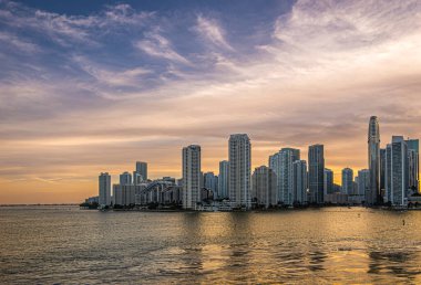 Miami, Florida, ABD - 29 Temmuz 2023: Geniş açı. Akşam 19: 43 'te Brickell Key Adası' ndaki binaların üzerinde gün batımı. Tequesta puanları ortada. Nehrin iki yakasında da sarı su var.