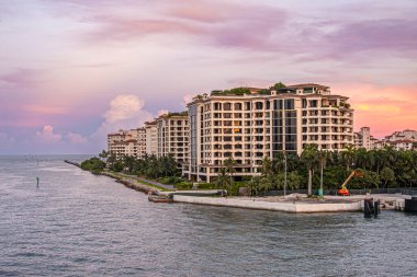 Miami, Florida, ABD - 29 Temmuz 2023 Fisher Island NE sahili boyunca lüks konutlar ve akşam gökyüzünün altında bir köşe. İnşaat yapılıyor. Deniz ve yeşil yapraklar