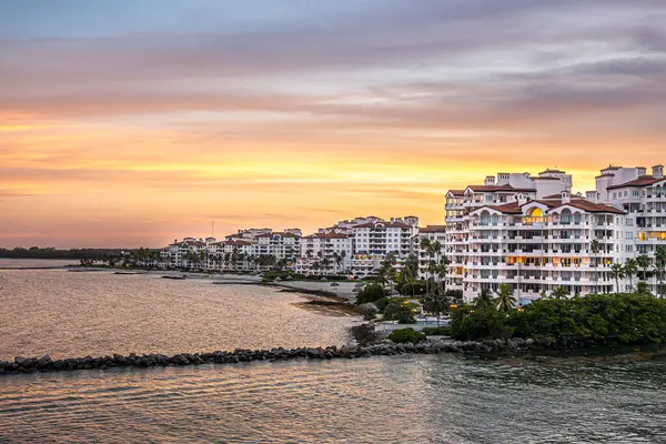 Miami, Florida, ABD - 29 Temmuz 2023: Portakal sarısı günbatımı gökyüzü, Fisher Adası 'nın lüks konutlarının kıyılarına bakıyor. Her köşede iskele ve yeşil yapraklar