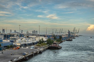 Miami, Florida, ABD - 29 Temmuz 2023: Liman, konteynır terminalinde uzun menzilli ön taraftaki römorkör, konteynırlı bahçe alanı, ufuktaki yüksek binalar, hepsi günbatımı bulutları altında