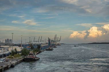 Miami, Florida, ABD - 29 Temmuz 2023 Harbor, konteynır terminali önünde römorkörle, konteynırlarla dolu bahçe alanı. Virginia Key Adası 'nın kuzey tarafında büyük gün batımı bulutu