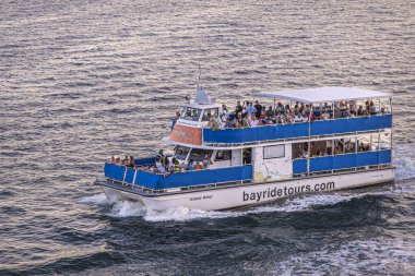 Miami, Florida, ABD - 29 Temmuz 2023: Bayridetours Ada Rüzgarı teknesi liman suyunu yansıtan gün batımı ışığına yakın çekim. Güvertede bir sürü insan var.