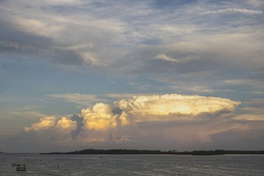 Miami, Florida, ABD - 29 Temmuz 2023 Virginia Key Adası üzerinde günbatımı bulutu ve mavi gökyüzünde ay var. Koyda bir tur teknesi. Atık su arıtma endüstrisi