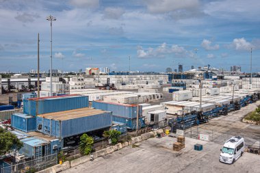 Miami, Florida, ABD - 29 Temmuz 2023: Liman terminalindeki konteynır yığınları mavi bulutların altında. Ufukta binalar olan geniş bir manzara. Yakınlarda bir karavan var.