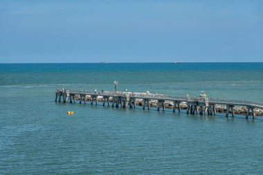 Liman Canaveral, Florida, ABD - 30 Temmuz 2023: Tahta kaldırımlı balıkçı iskelesi mavi Atlantik Okyanusu 'na uzanıyor. Yayalar ve aktif balıkçılar mevcut. Mavi gökyüzü. Gemi ufukta görünüyor.