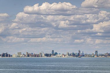 New York, New York, ABD - 1 Ağustos 2023: Mavi bulutlar altında Coney Adası plajında kulesi ve tekerleği olan Maimonides Park. Önde gri okyanus suyu var. Binaların kemeri,