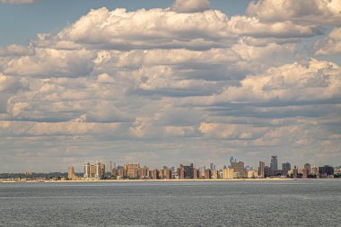 New York, New York, ABD - 1 Ağustos 2023: Coney Adası SW kıyı şeridi yoğun yüksek bina kemeriyle mavi bulutların altında ince kum hattının arkasında