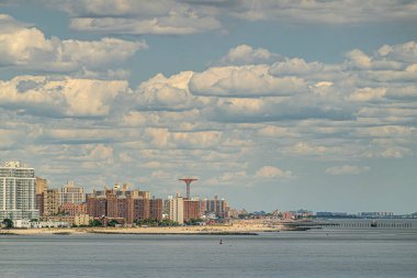 New York, New York, ABD - 1 Ağustos 2023 Coney Adası 'nın kumlu sahilinden Maimonides eğlence parkı kulesi ve mavi bulutların altındaki yüksek binalardan oluşan bir duvar