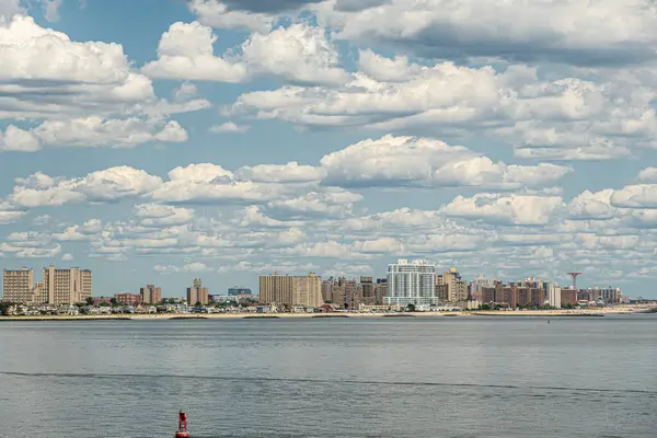 stock image New York, NY, USA - August 1, 2023: Coney Island coastline from west to Maimonides amusement park under blu cloudscape. Tall buildings form wall. Beach line up front