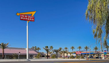 Las Vegas, NV, ABD - 12 Mayıs 2024: Batı Russell yolundaki Allegiant Stadyumu 'nun karşısındaki mavi gökyüzüne karşı renkli IN-N-Out BURGER fast food ve logo tabelası. Polaris Caddesi 'ndeki sembol benzin istasyonu.