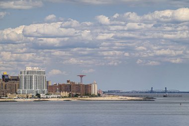 New York, New York, ABD - 1 Ağustos 2023: Coney Adası plajı ve Gil Hodges Memorial Köprüsü arkada mavi bulutların altında. Maimonides Park Kulesi yüksek bina duvarına bakıyor.