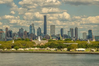 New York, New York, ABD - 1 Ağustos 2023: Yukarı Körfez 'deki Yeşil Valiler Adası batı kıyı şeridi ve Liggett Hall' un tepesinde Brooklyn liman vinçleri ve mavi bulutların altındaki yüksek binalar