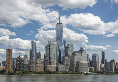 New York, New York, New York, ABD - 1 Ağustos 2023: Hudson Nehri 'ndeki NW' den Finans Bölgesi 'ne bakın. Bir Dünya Ticaret Merkezi gökdeleni mavi bulutların altında hüküm sürüyor. Sahilde yeşil ağaç sınırı