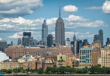 New York, New York, ABD - 1 Ağustos 2023: Bir Vanderbilt, Empire State, ve Chrysler gökdelenleri Hudson Nehri 'nden mavi bulutların altında görüldü. Yeşil kıyı şeridi,