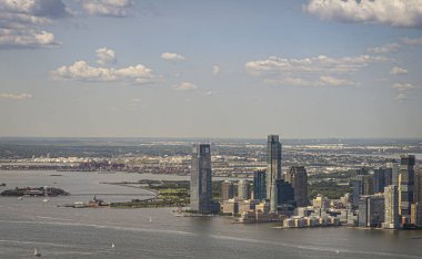New York, New York, ABD - 2 Ağustos 2023: Jersey City kıyıları Esses 1 'den kuzey Hudson nehrinin yukarısındaki karanlık kuleye Hyatt naip rıhtımını ve Empire State Binası' ndan görüldüğü üzere mavi bulutların altındaki apartmanlar