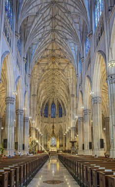 New York, New York, ABD - 2 Ağustos 2023: Gotik Aziz Patricks Katedrali, naf ve kahverengi ahşap banklar arasında sunakla girişten şansa kadar iç görünüm. Tavanı destekleyen uzun sütunlar ve kemerler