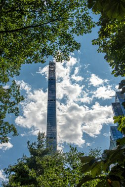 New York, New York, ABD - 2 Ağustos 2023: Steinway Kulesi mavi bulutların altında yeşil yapraklar arasında Central Park 'tan görüldü