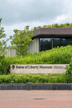 New York, New York, ABD - 4 Ağustos 2023: Gri bulutlar altında bina önündeki Özgürlük Heykeli isim tabelası. Yeşil yaprak