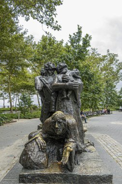 New York, New York, ABD - 4 Ağustos 2023: Battery Park 'ta Luis Sanguino tarafından yapılan göçmen anıtı. Arkadaki yeşil yapraklar.