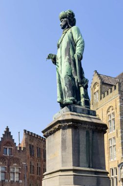 Brugge, Flanders, Belçika - 25 Haziran 2024: Ressam Jan Van Eyck heykeli, mavi gökyüzüne karşı yeşil bronz.