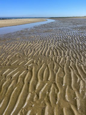 Knokke-Soygunu, Flanders, Belçika - 24 Haziran 2024: Islak kum dalgaları Kuzey Denizi Sahili 'nde gözün alabildiğince mavi sabah gökyüzünün altında.