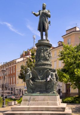 Trieste, İtalya - 27 Haziran 2024: Habsburg Piazza Venezia 'daki Maximilian heykeli. Boyalı cepheler ve arkada yeşil yapraklar.