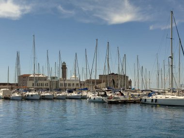 Trieste, İtalya - 27 Haziran 2024: Molo Teresiano ve binaları ve önlerinde büyük yelkenli yatları bulunan ışık kulesi feneri