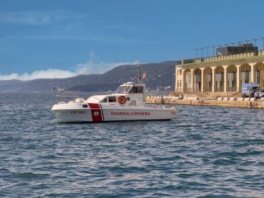 Trieste, İtalya - 27 Haziran 2024: Mavi bulutların altında küçük bir sahil güvenlik botu seyir terminalinin bir kısmıyla yakın plan. Ufuktaki yeşil orman tepeleri