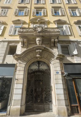 Trieste, İtalya - 29 Haziran 2024: 3. Via Amilcare Ponchielli binasının anıtsal girişi baş heykeli ve heybetli balkonu gösteriyor. Satış mağazaları zemin katta