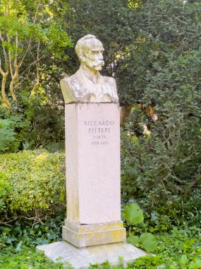 Trieste, Italy - June 29, 2024: Riccardo Pitteri statue set among green foliage in park named Giardino Pubblico Muzio de Tommasini clipart