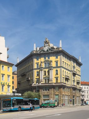 Trieste, İtalya - 29 Haziran 2024: Piazza Guglielmo Oberdan 'daki Palazzo Arrigoni anıtsal tarihi binasının ön cephesinde çeşitli sanat eserleri var, üstte heykeller, mavi bulutların altındaki köşelerde sütunlar