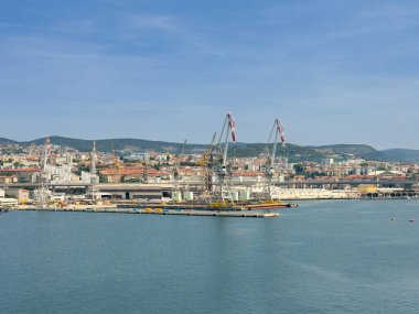 Trieste, İtalya - 29 Haziran 2024: Ticari liman. Rıhtımda gemileri olmayan büyük turnalar. Şehir manzarası ve dağ sırası ufukta