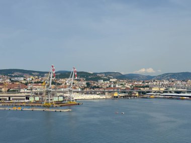 Trieste, İtalya - 29 Haziran 2024: Ticari liman. Rıhtımda gemileri olmayan büyük depo binaları. Şehir manzarası ve dağ sırası ufukta