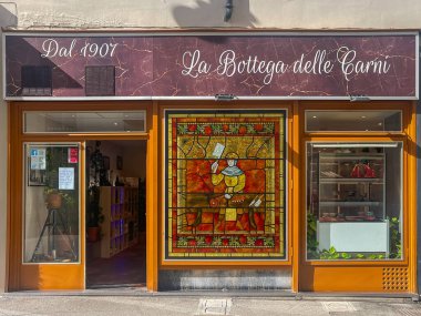 Trieste, Italy - June 29, 2024: La Bottega delle Carni in Via Amilcare Ponchielli, front facade, is butcher store with large stained glass painting of man with ax cutting pieces of meat clipart