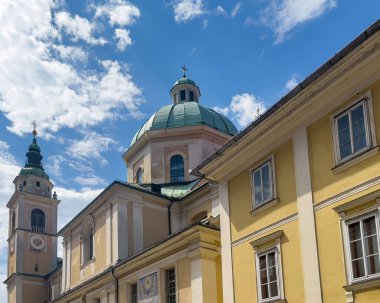 Ljubljana, Slovenya - 28 Haziran 2024: Saint Nicholas Katedrali 'nin güney cephesi ve Ciril-Metodov alışveriş caddesinden mavi bulutların altında saat kulesi. 