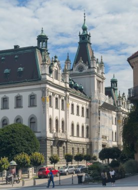 Ljubljana, Slovenya - 28 Haziran 2024: Slovenya tarihi üniversite binası batı cephesi Vegova ulica caddesinde saat kulesiyle. Yayalar ve arabalar burada. Mavi bulut