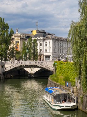 Ljubljana, Slovenya - 28 Haziran 2024: Ulusal Halk Sağlığı Enstitüsü (NIJZ) mavi bulutlar altında beyaz-gri bina. Neptün 'ün yan binadaki heykeli. Ljubljanica nehri. Yapraklar ve tur teknesi