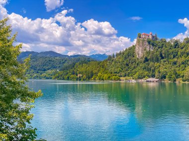 Slovenya 'nın Bled Gölü - 28 Haziran 2024: Şato ve müze, kayaların tepesinde, yeşil ormanlarla çevrili beyaz kayalıklarıyla. Şato Havuzu ve göldeki kürek kulübü.