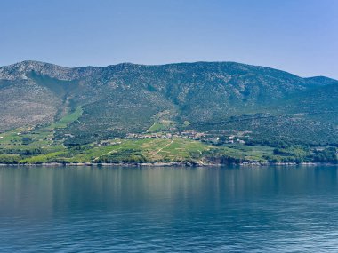 Korcula, Hırvatistan - 30 Haziran 2024: Anakaranın karşısında, adanın kuzeyinde post-up Vineyards. Adriyatik 'e yakın yeşil üzüm bağları olan uzun, geniş bir dağ kanadı. Kırmızı çatılı evleri olan küçük bir yerleşim yeri