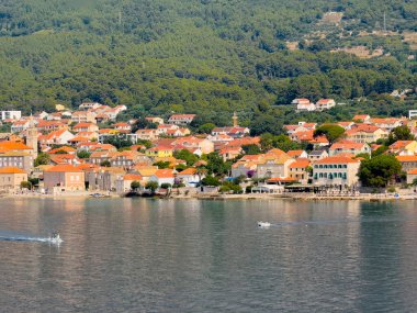 Orebic, Croatia - June 30, 2024: Church of Mary help of Christians towers over the town and hotels and restaurants on Adriatic Sea shoreline, all set in red roofed cityscape. Forested mountain flank in back clipart