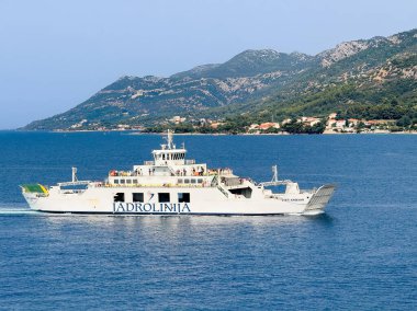 Korcula, Hırvatistan - 30 Haziran 2024: Korcula ve Orebic kasabaları arasında mavi Adriyatik Denizi üzerindeki Jadrolinija feribot hattı. Dalmation anakarasında yeşil ormanlı dağ kanatları,
