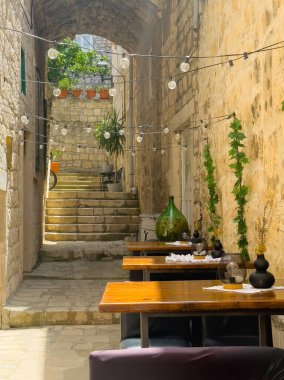Korcula, Hırvatistan - 30 Haziran 2024: Kapetan Vjeko restoranının masaları dışarıda. Yukarıdaki kırmızı saksılarda yeşil bitkiler