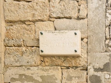 Korcula, Croatia - June 30, 2024: Don Luke Depola alley name sign on old stone wall clipart