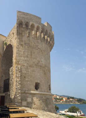 Korcula, Croatia - June 30, 2024: Kanavelic Tower against blue sky. Restaurant tables in corner clipart